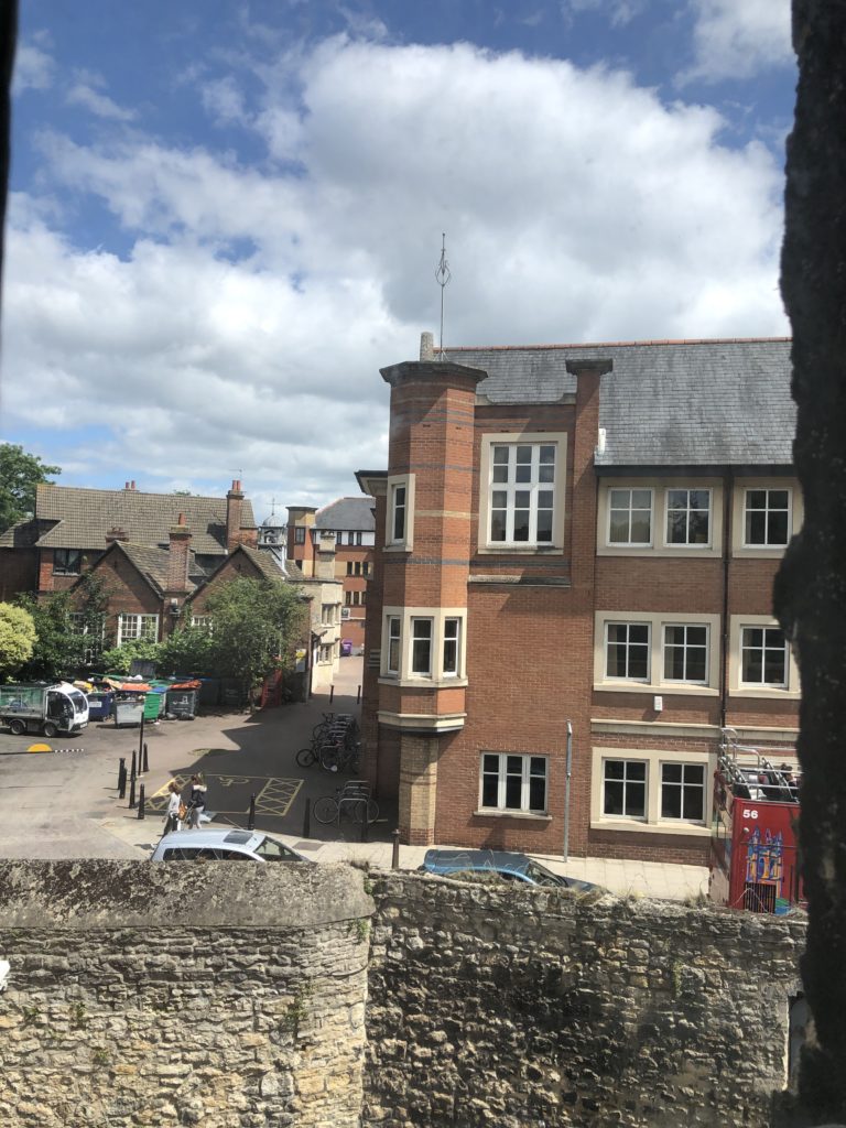 A red brick building and low wall as seen outside of a two story window